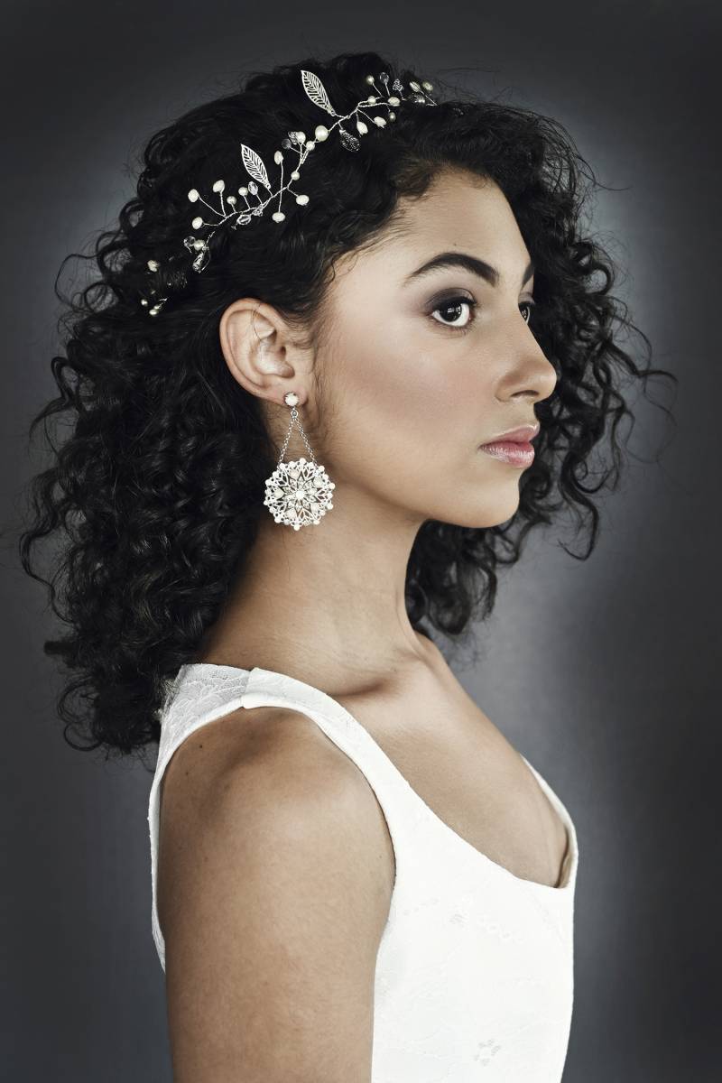 Profile of woman with black curly hair with bridal crown and large round hanging earrings 