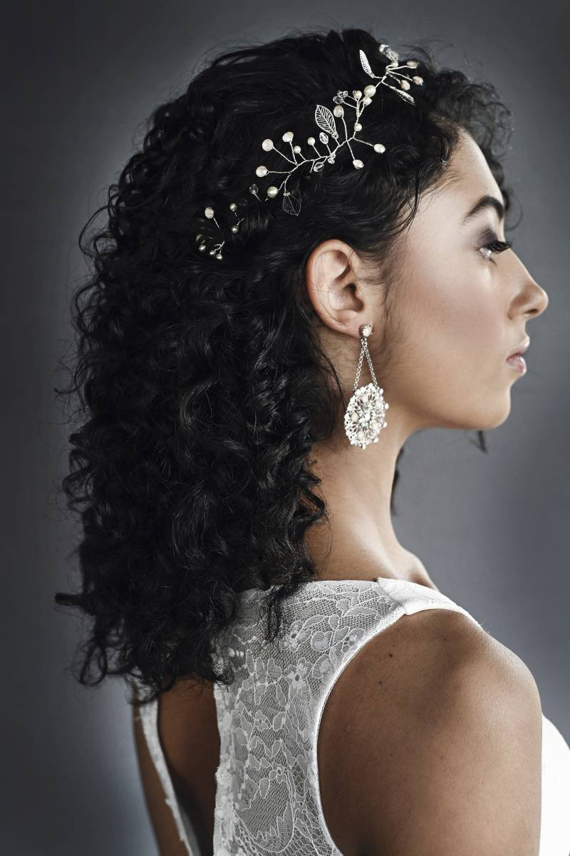 Profile of woman with black curly hair with bridal crown and large round hanging earrings 