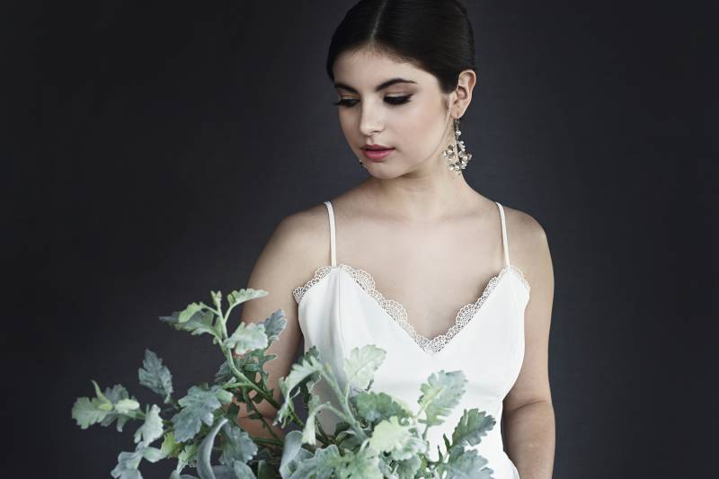 Woman in white dress and hanging earrings behinds green plant 