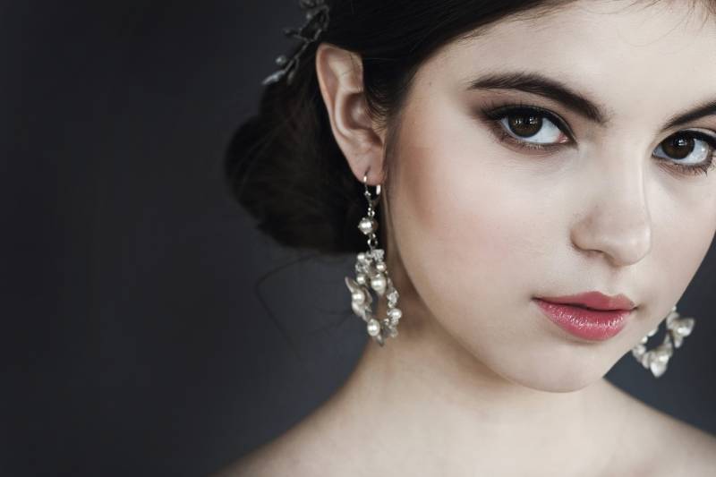 Face of woman with black hair in bun and large hanging earrings 