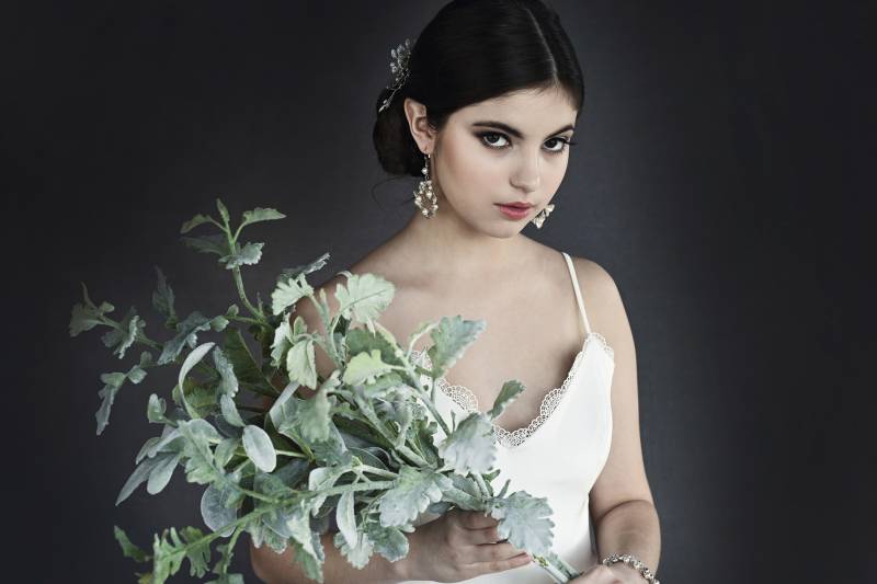 Woman in white dress and black hair in a bun holding green plant
