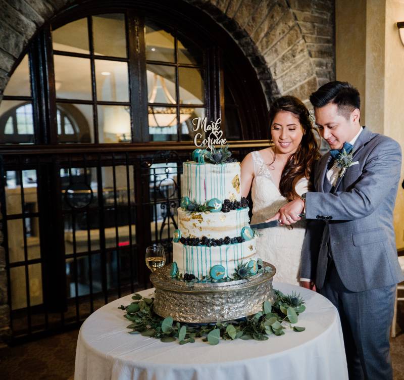 Bride and groom cut large blue and white wedding cake together smiling 