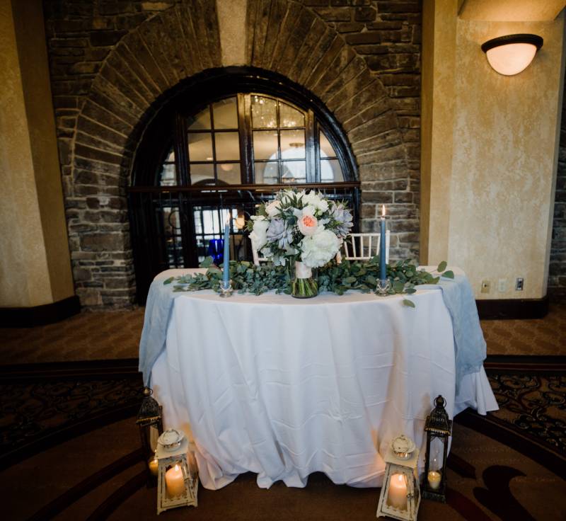Small white table with white and blush centerpiece and blue candlesticks with lanterns around 