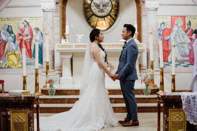 Bride and groom holds hands facing each other at front of church candles beside 