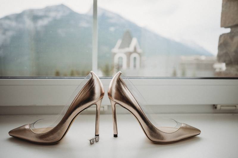 Gold heels facing opposite directions on window sill looking onto mountains 