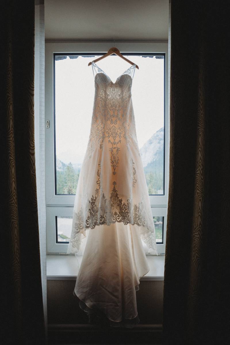 White lace wedding dress hanging from window with curtains to side