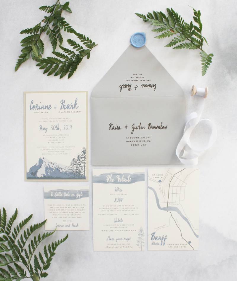 Wedding invitation flat lay with grey envelope and powder blue accents ferns around 