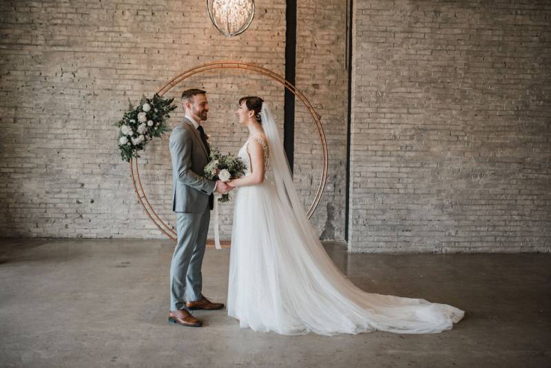 Man and woman hold hands in front of copper wedding arch and chandelier 