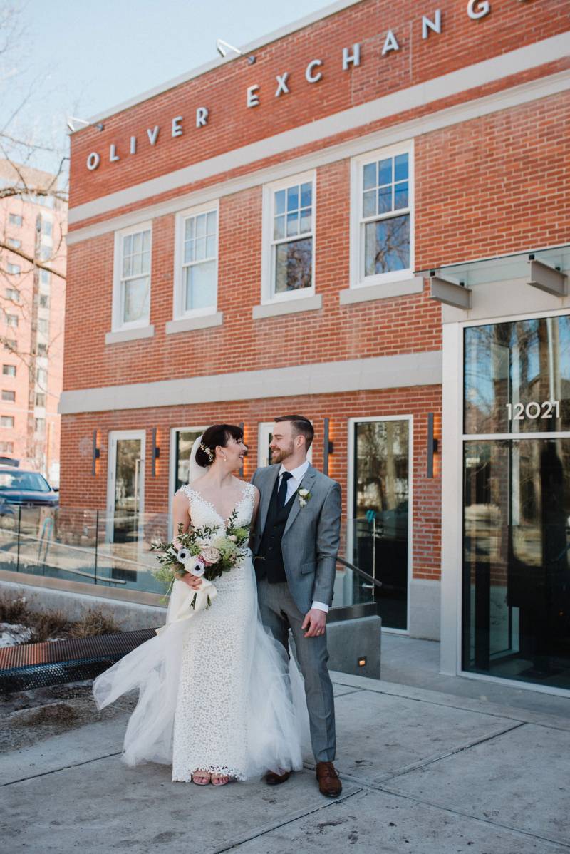 Bride and groom smiling at each other in front of red brick building