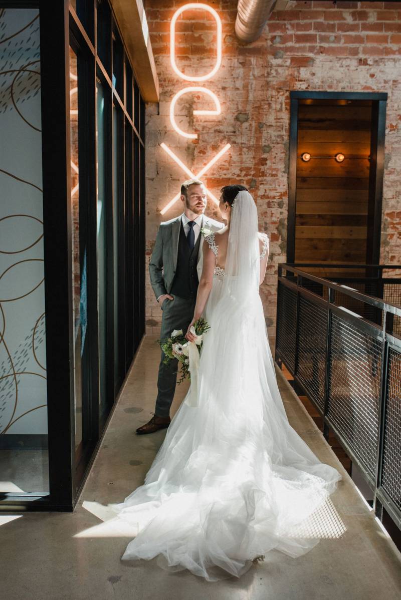 Bride and groom face opposite with glowing neon sign on brick wall 
