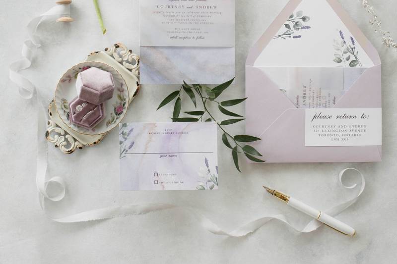 Wedding invitation flat lay with lavender envelope and suede ring box and white ribbon