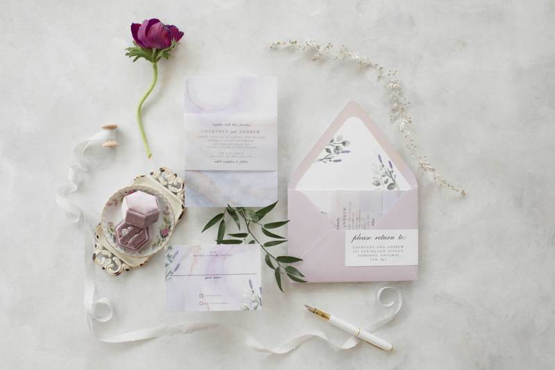 Wedding invitation flat lay with lavender envelope purple flower and suede ring box and white ribbon