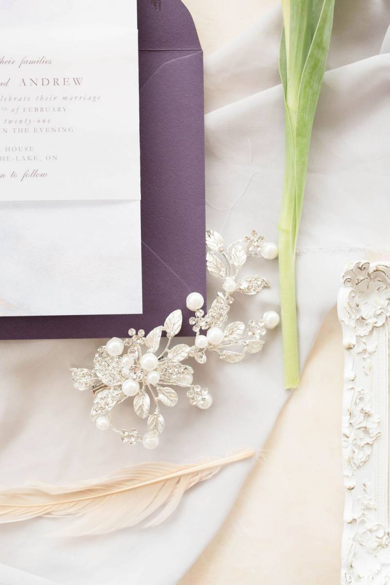 Purple envelope beside flower stem and pearl white hair clip 