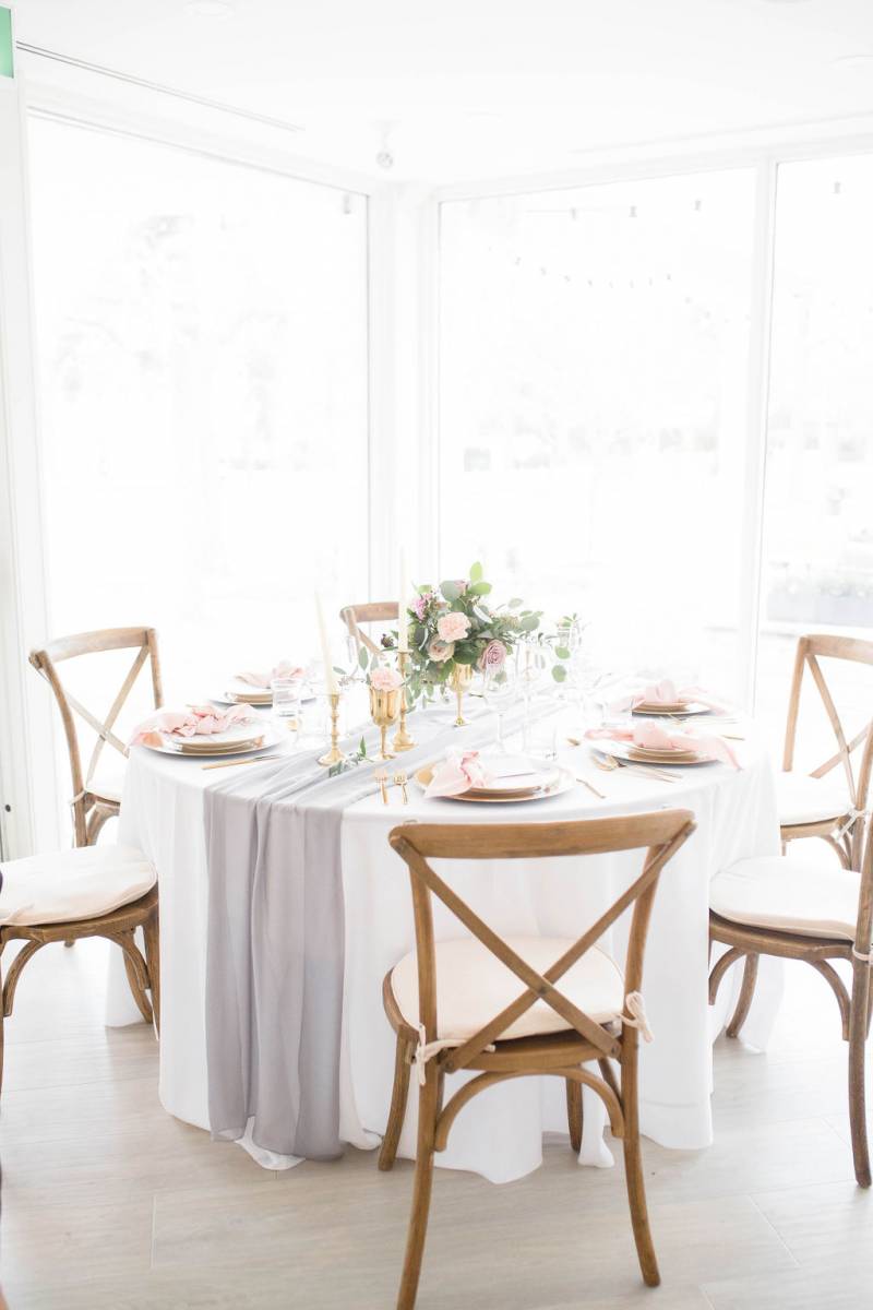 Wooden chairs around small white table with blush floral centerpiece 