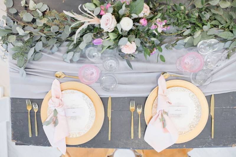 Table setting with gold plates and gold cutlery with green table runner and floral centerpiece