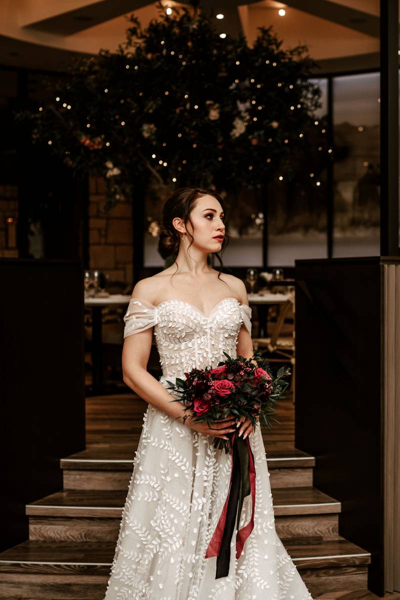 Woman in white lace dress holding burgundy bouquet looking to side 