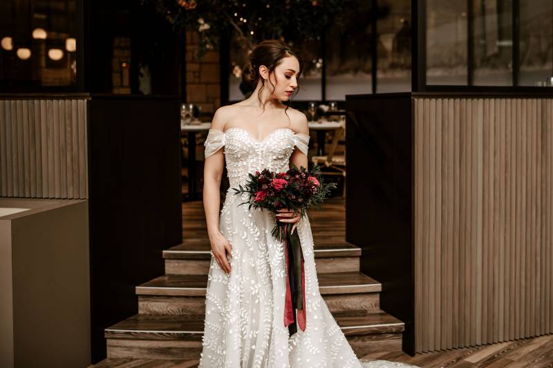 Woman in white lace dress holding burgundy bouquet looking to side 