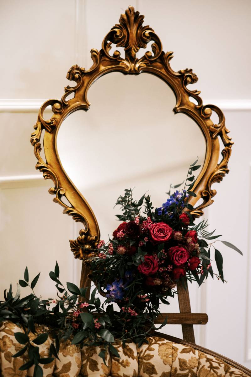Gold edged mirror with red and blue floral arrangement on bottom 