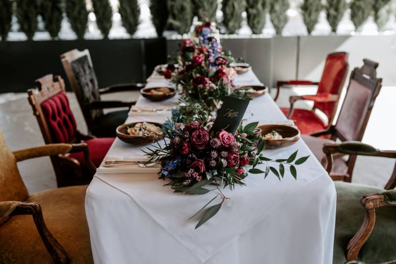 small white table with mismatched seats surrounding and large red and blue floral arrangements  