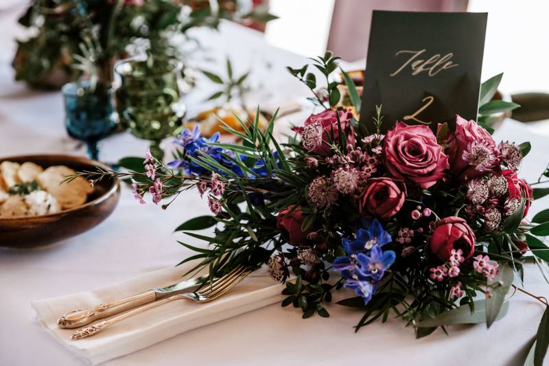 Dark red and blue floral arrangement on white table with black card 