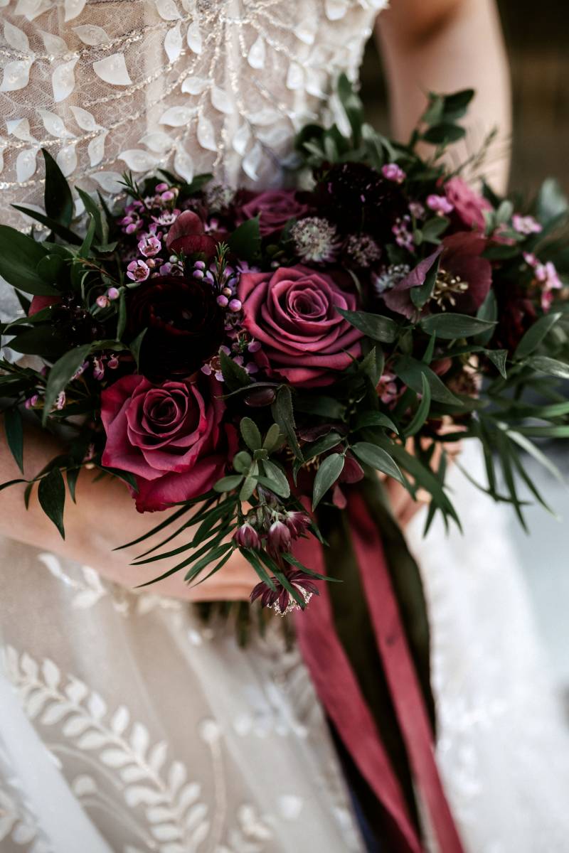 Burgundy bouquet hold by woman in white lace dress 