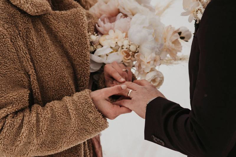 Bride fits wedding ring onto grooms finger in fuzzy brown coat