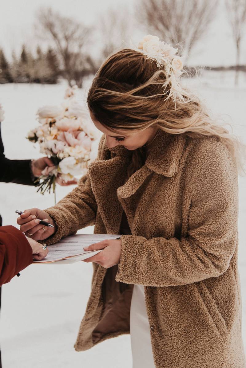 Bride writing on paper wearing fuzzy overcoat 