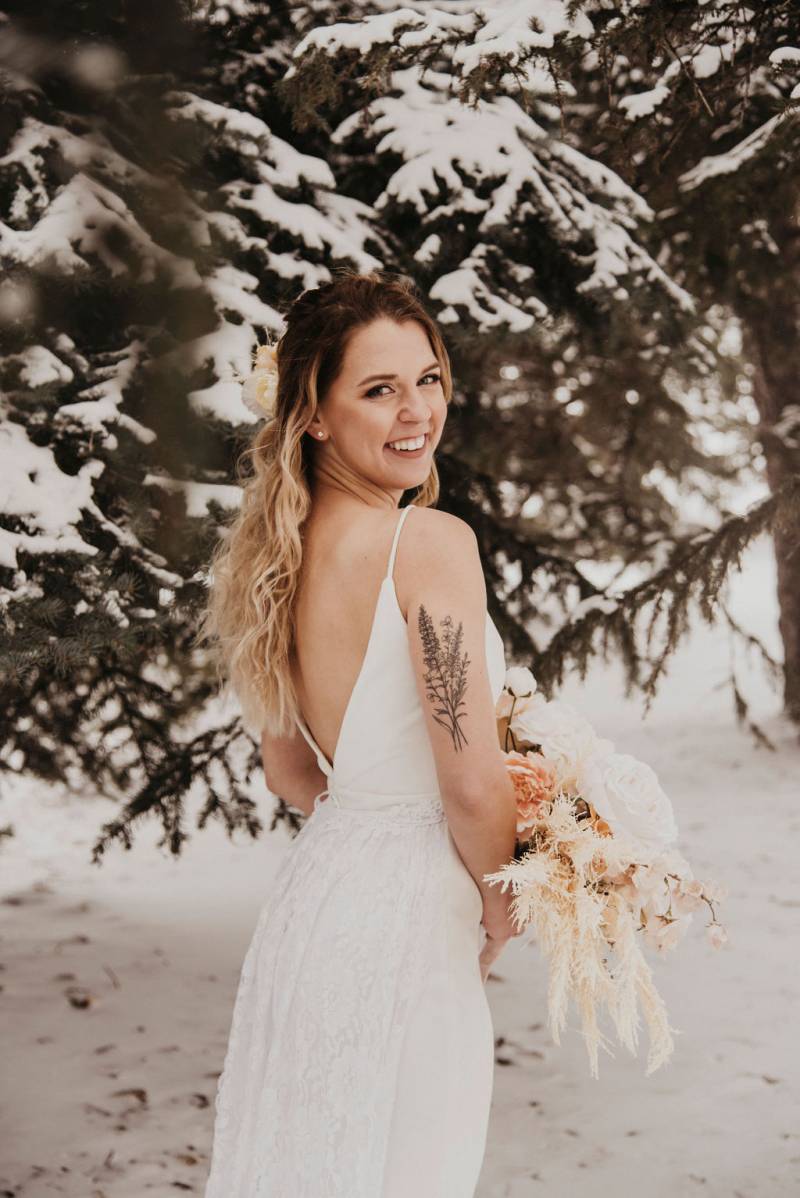 Bride turned away facing forward in white open back dress holding pale pink and white bouquet