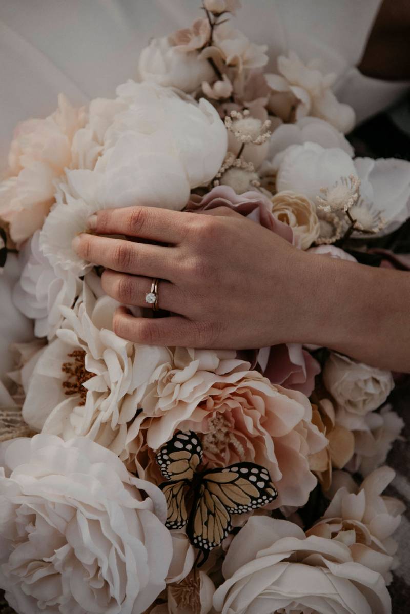 Bride laying hand with ring on pale pink and white bouquet with butterfly 
