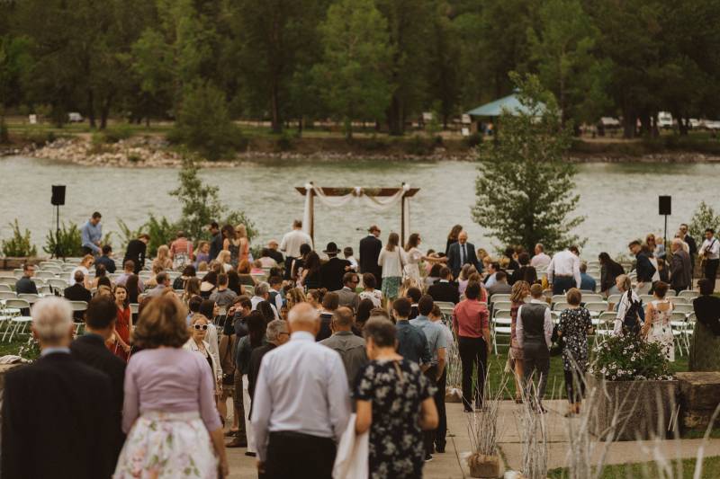 Guests walking towards seating in front of wedding arch and river