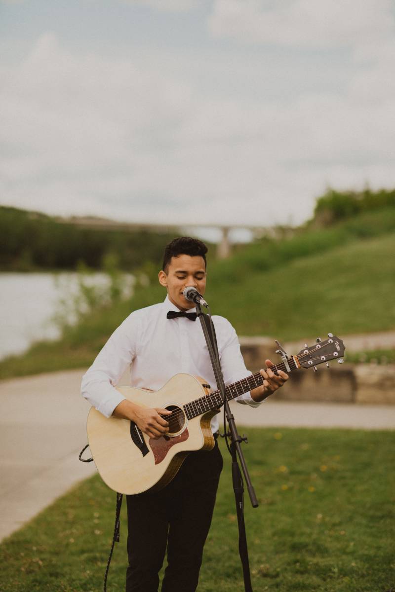 Man in white shirt and bowtie plays acoustic guitar and sings into microphone