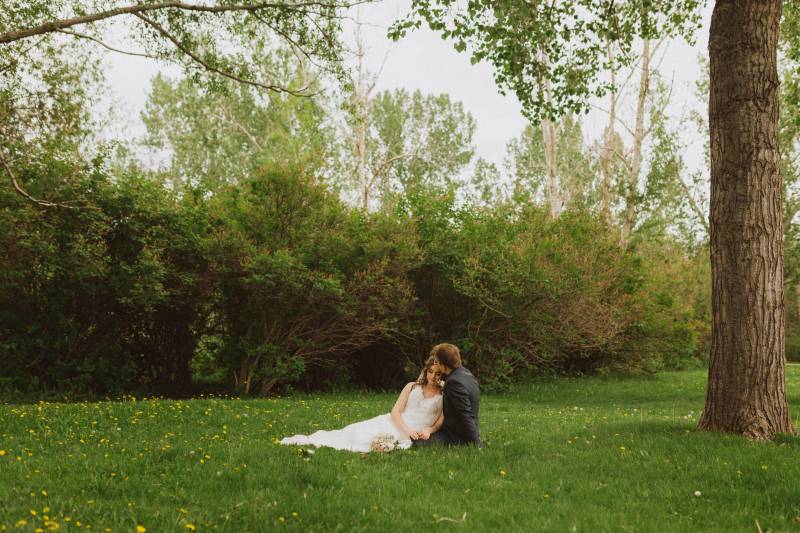 Bride and groom sit together in grassy field 