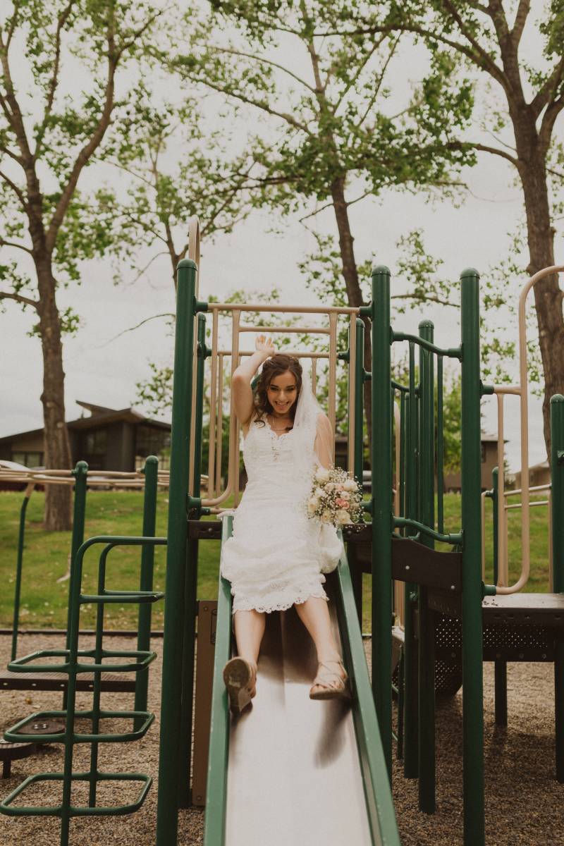 Bride smiling holding bouquet sliding down green park slide 