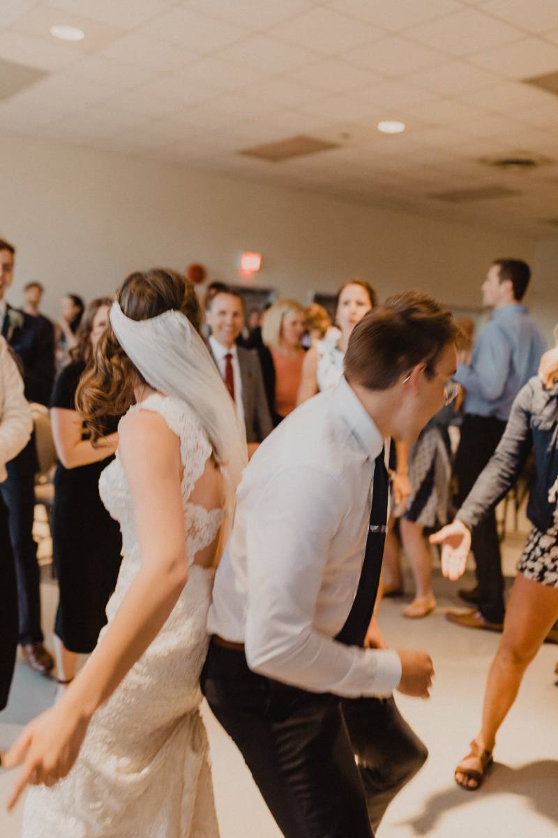 Bride and groom dance with backs together and guests surrounding 