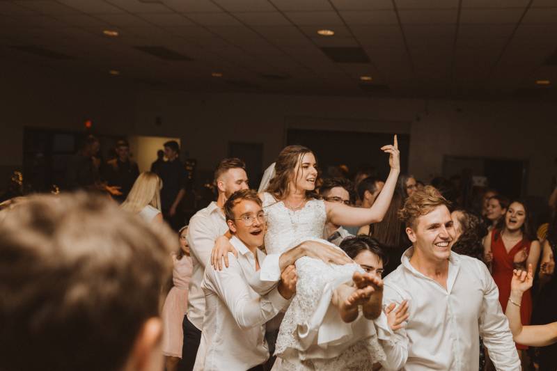 Bride carried by groomsmen while pointing to the ceiling 