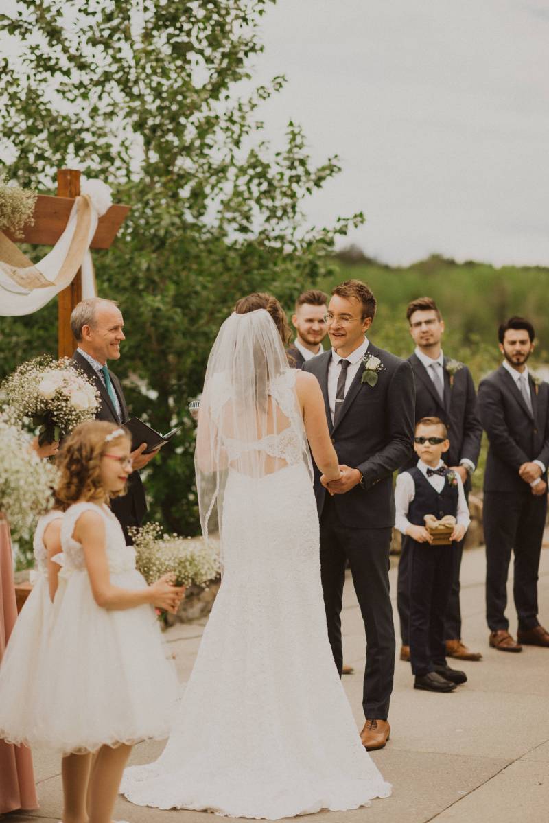 Bride and groom stand holding hands in front of officiant and guests of honor 