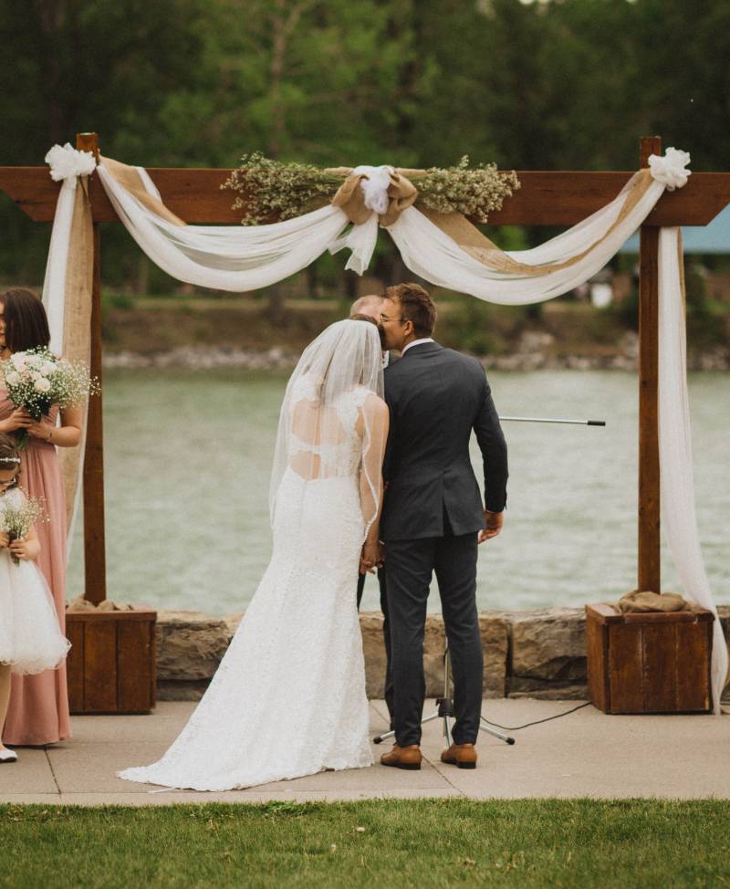 Bride and groom face wedding arch with hanging white fabric and river 