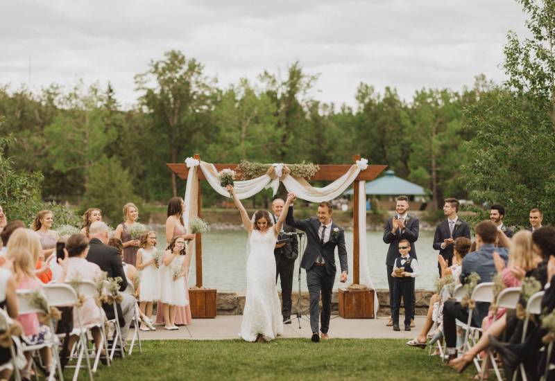 Bride and groom walk down aisle hands raised while guests applaud 