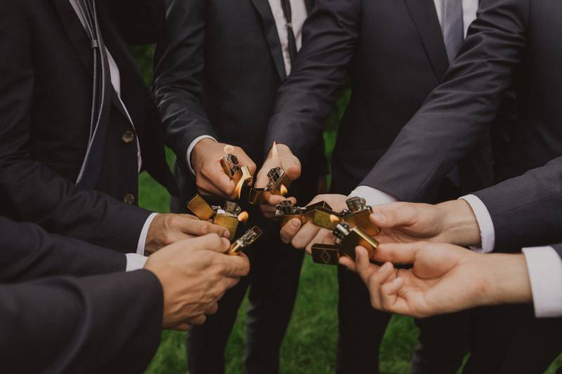 Groom and groomsmen stand in circle holding lit gold lighters 