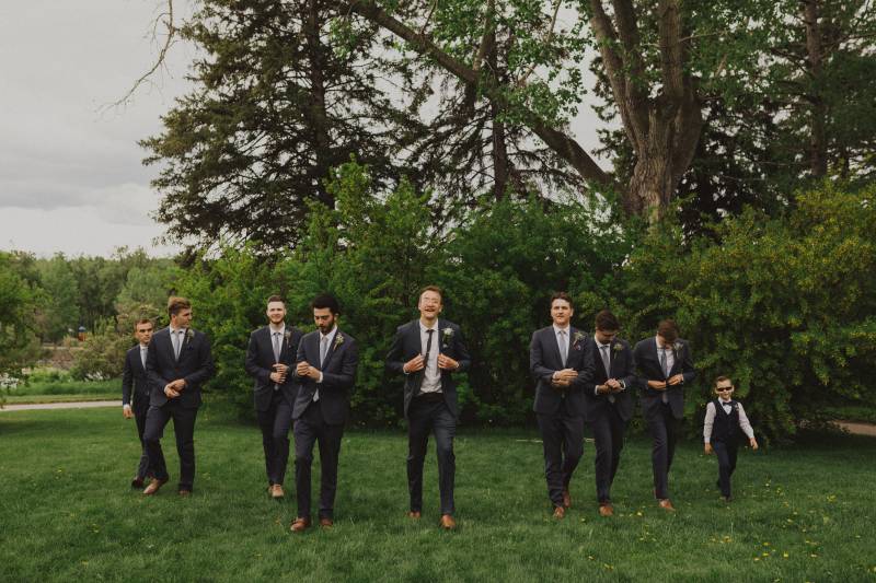 Groom and groomsmen walk adjusting jackets in grassy field 