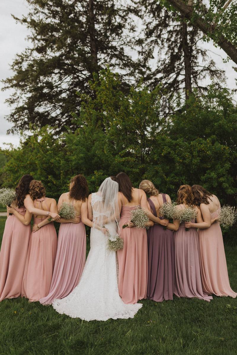 Bride and bridesmaids face away holding bouquets behind backs in arms
