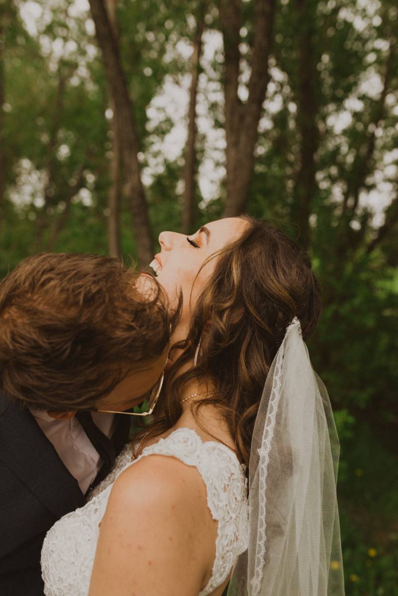 Groom kisses brides neck smiling in forested area