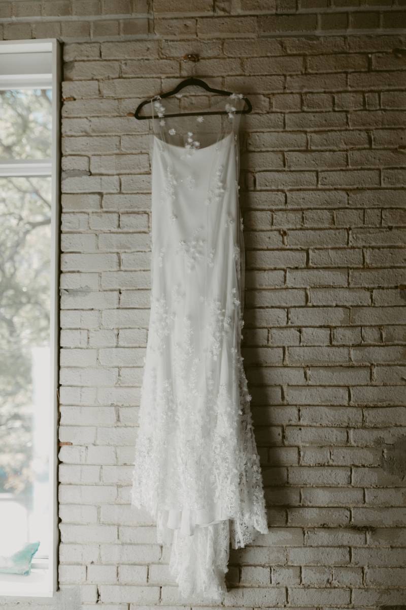 White dress with white embroidered flowers hanging on brick wall