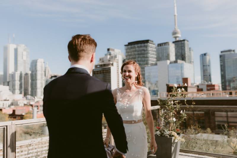 Bride and groom stand facing each other smiling on terrace facing city 