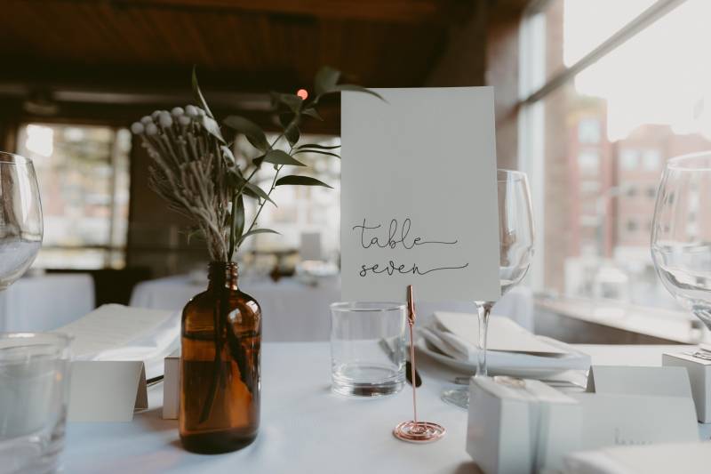 Table setting and number with white and green floral centerpiece in brown bottle 