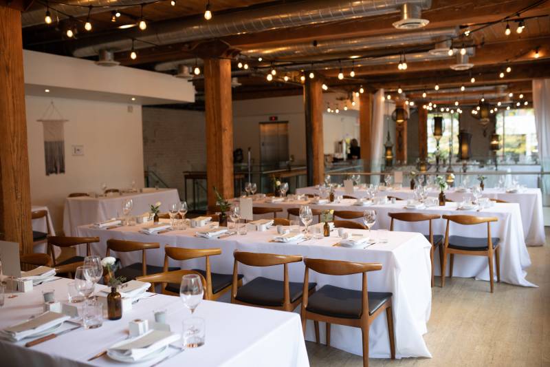 Wedding reception in long room with large wooden support beams and fairy lights over long white tables 