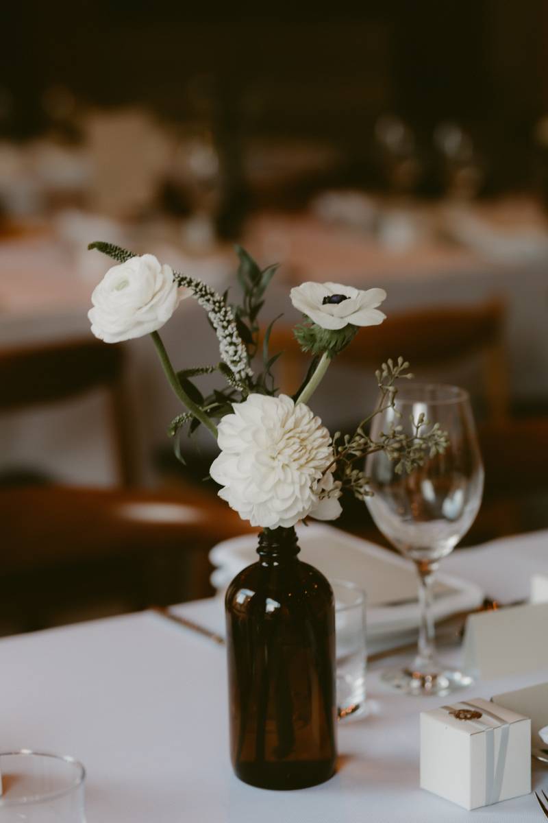 white and green floral centerpiece in brown bottle beside table scape