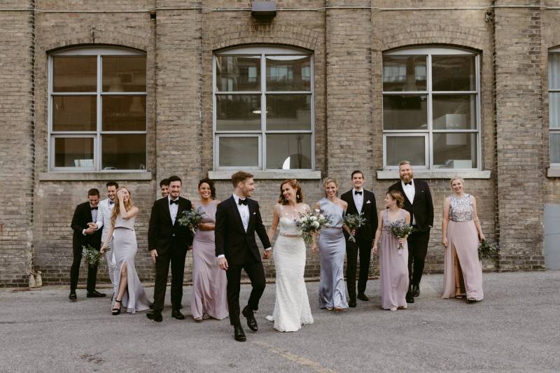Bride and groom with bridesmaids and groomsmen outside brick building walk in line 