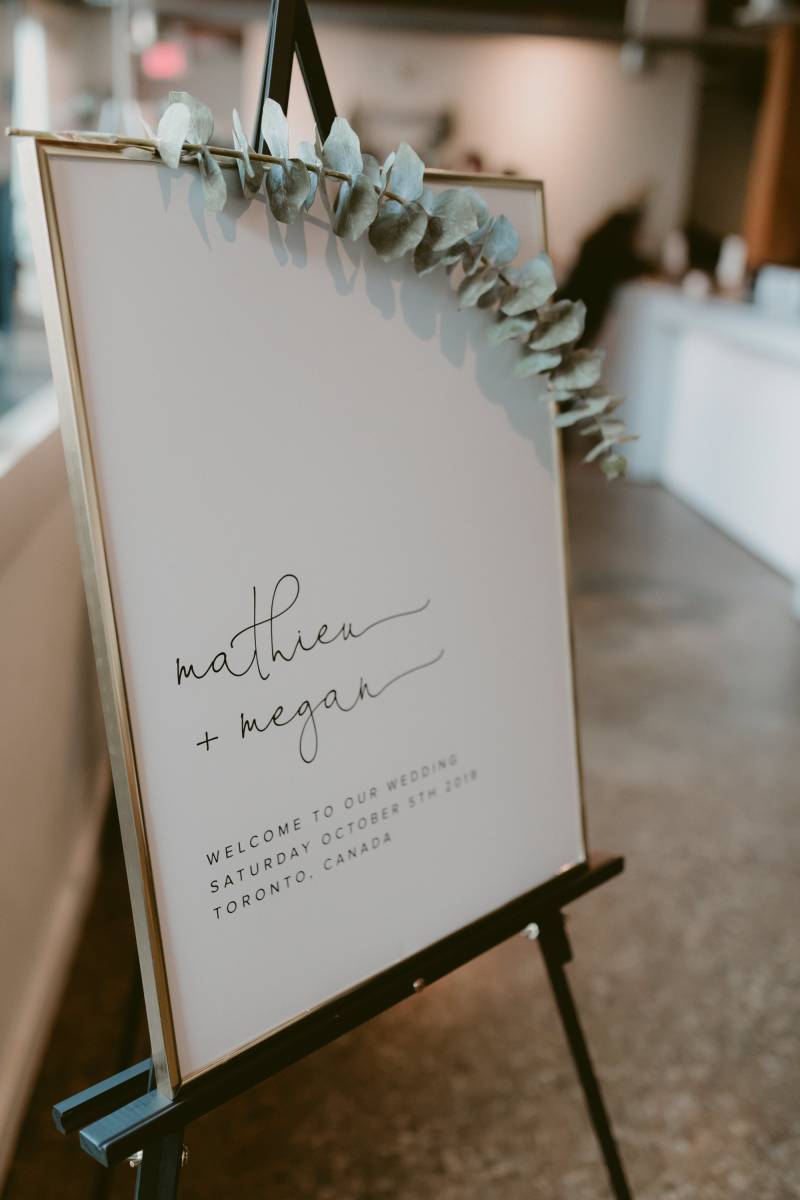 Wedding reception sign with gold border and leafy green accent on black easel 