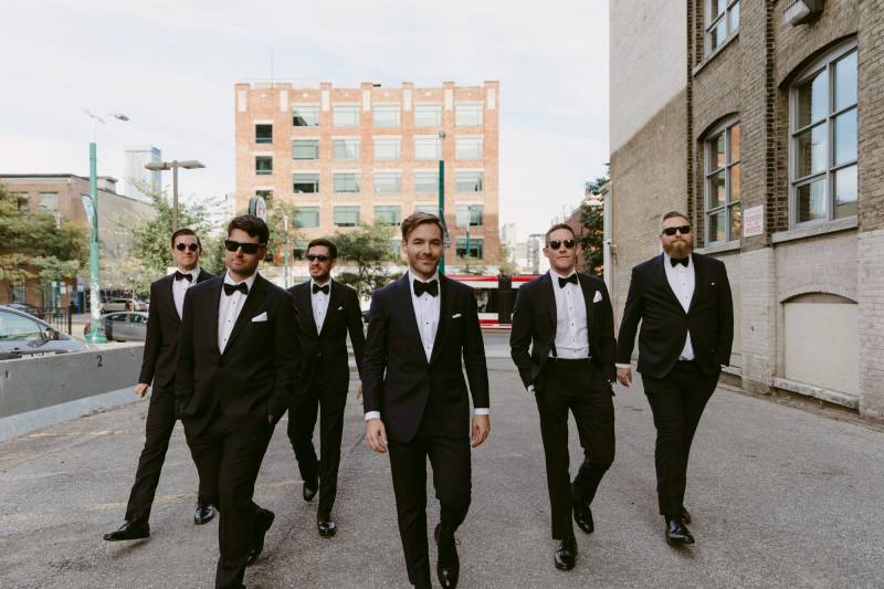 Groom and groomsmen walk together outside brick building 